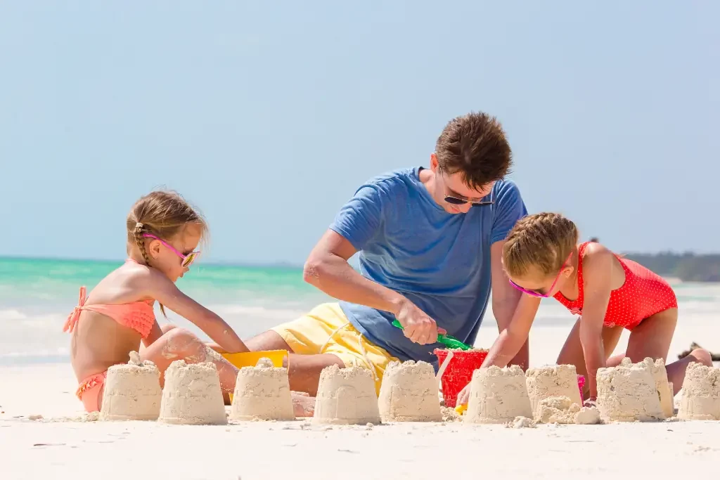 Vater baut mit Kindern eine Sandburg am Meer