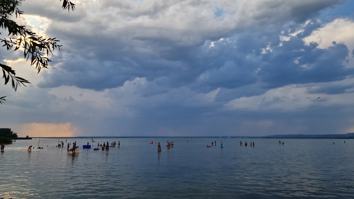 Badende stehen weit draußen im flachen Wasser des Balaton, Gewitterwolken am Himmel