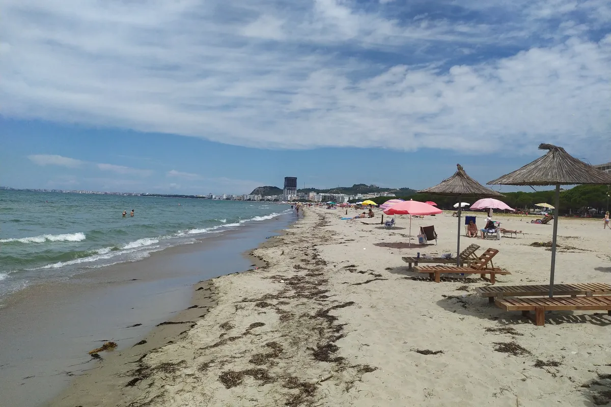 Sandstrand von Golem bei Durrës mit Strohschirmen und Holzliegen, Hochhäuser von Durrës im Hintergrund