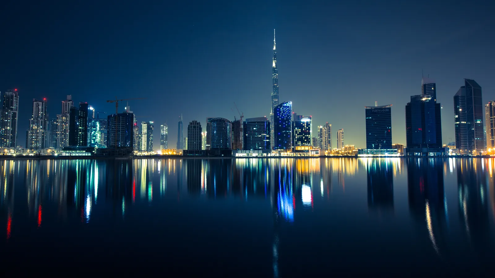 Skyline von Downtown Dubai mit dem Burj Khalifa bei Nacht, gespiegelt im Wasser