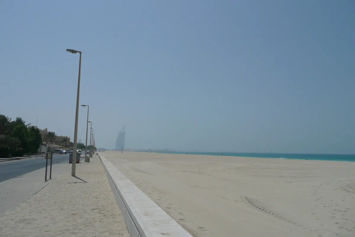 Leerer Sandstrand am Jumeirah Beach in Dubai, im Dunst dahinter der Burj Al Arab