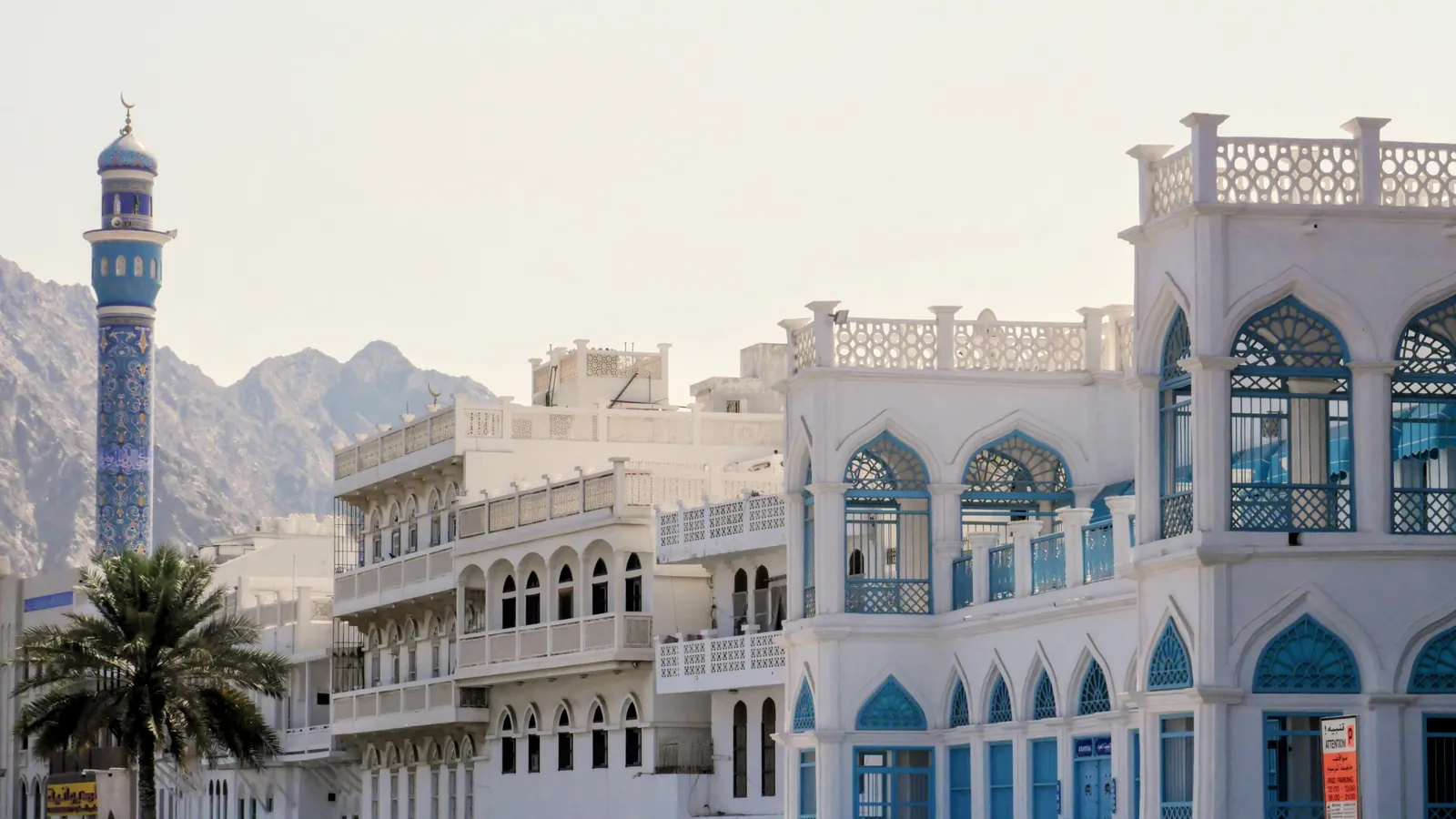 Beste Reisezeit für den Oman mit Kindern: weiße Häuser und Minarett an der Muttrah-Corniche in Maskat, dahinter Berge