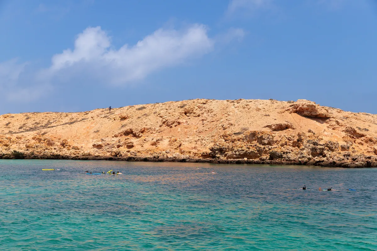 Schnorchler im türkisfarbenen Wasser vor einer felsigen Insel der Daymaniyat bei Maskat